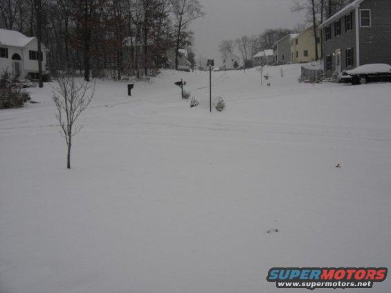 Dark sedan covered in snow parked in front of a house on a snowy day