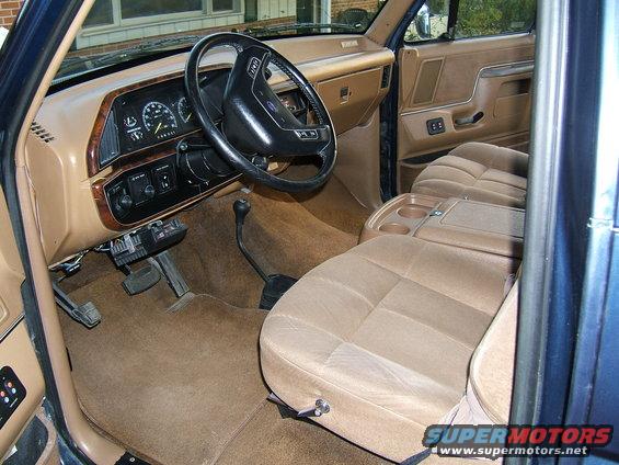 Tan cloth interior of a 1987 Ford Bronco with a four-spoke steering wheel and column shifter