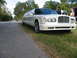 1997 Ford Crown Victoria - A long white limousine is parked on the side of a road, with people standing near the open front passenger door.