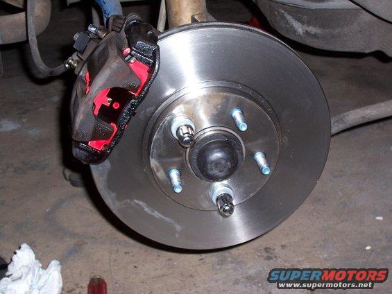 Close-up of a car's brake rotor and caliper assembly. The caliper is painted black with red accents