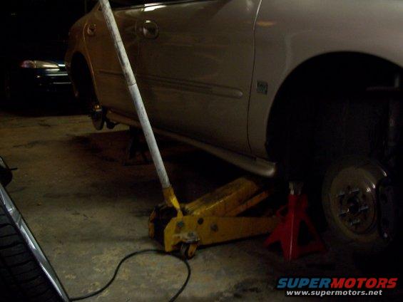 Silver sedan on jack stands with a yellow floor jack, rear wheel removed