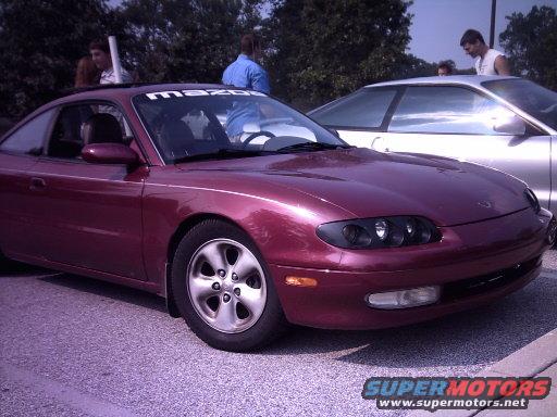 Maroon Mazda MX-6 coupe parked next to a silver car, with 'mazda' banner on windshield