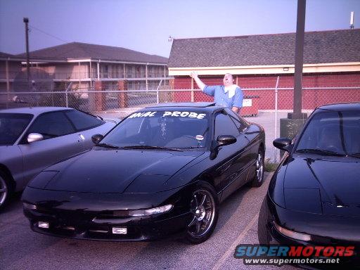 Black Ford Probe with a person in the sunroof, parked next to another Probe