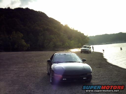 Black 1995 Ford Probe parked by a lake with pop-up headlights visible