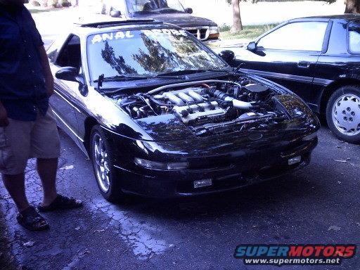 black sports car with engine exposed, parked next to another black car. Person standing nearby
