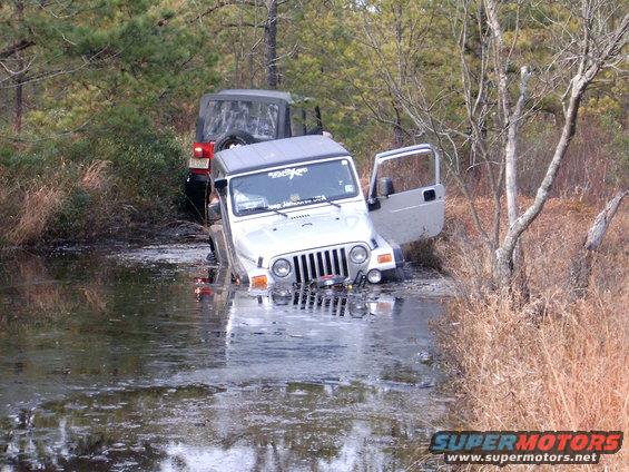 Silver Jeep Wrangler partially submerged in water with door open, red Jeep Wrangler behind it in water