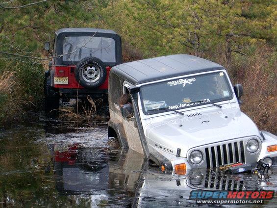 Two Jeeps are partially submerged in water. One is silver with 'Rubicon' visible, the other is red