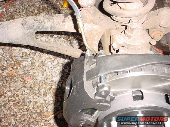 Close-up of a vehicle's front brake caliper and rotor assembly, with suspension components visible above