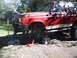 1990 Ford Bronco - A red 1990 Ford Bronco with a tan stripe is raised on jack stands for maintenance.
