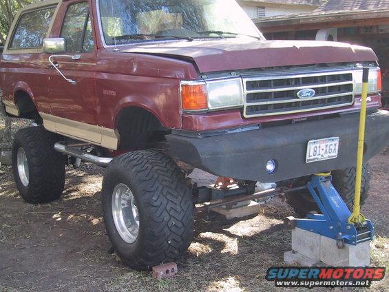 1990 Ford Bronco lifted with large tires, front view, jacked up
