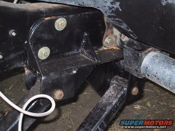 Black painted vehicle frame with bolts and suspension parts. A white braided hose is visible