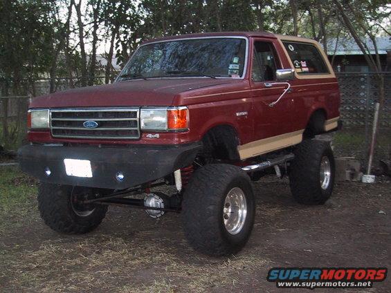 Lifted red Ford Bronco with tan trim, big tires, and aftermarket bumper