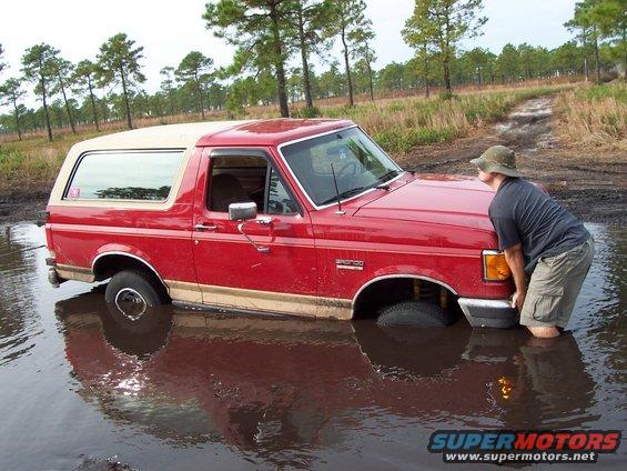 Red SUV stuck in mud, person pushing