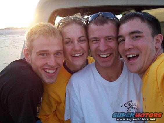 Four friends smiling for a selfie in the back of a vehicle at the beach