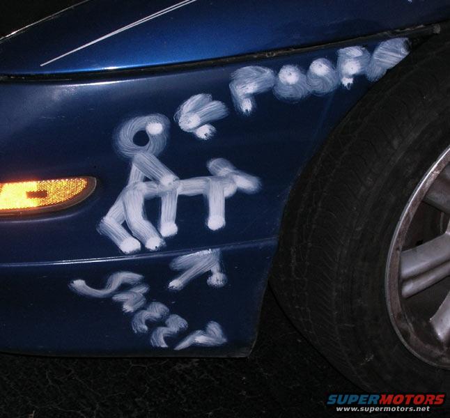 1993 Ford Probe fender with white graffiti depicting figures and the word 'Sheer'