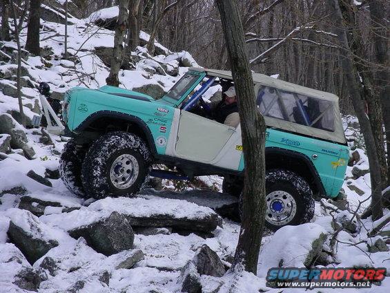 1969 Ford Bronco climbing rocky terrain in snow, turquoise and white paint, roll cage