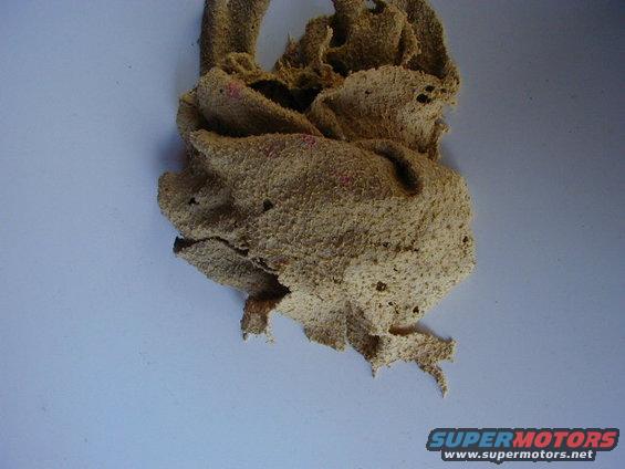 Torn, beige car part with pink specks against a light blue background