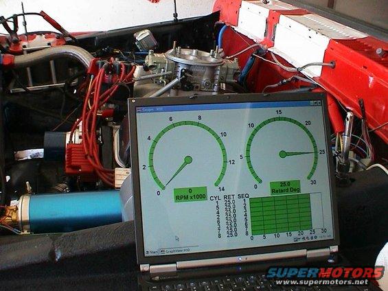 Engine bay with red wiring, blue canister, and carburetor, connected to a laptop showing RPM and retard degree gauges