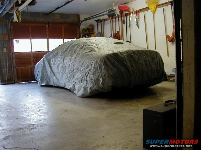 Car covered by a gray tarp in a garage with tools on the wall and a closed garage door