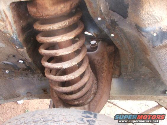 Close-up of a rusty coil spring and shock absorber assembly on a vehicle's undercarriage