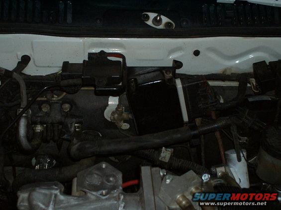 Engine bay with various hoses, wires, and black plastic components visible