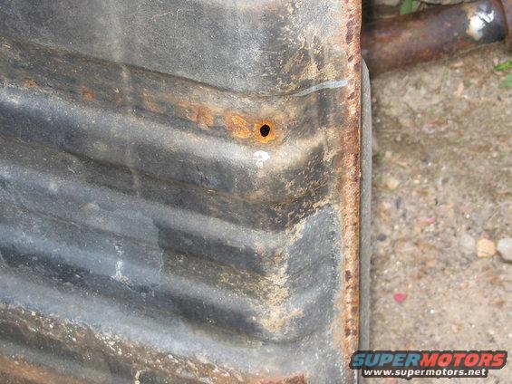 Corrugated metal part with rust and a hole, showing horizontal ridges and textured surface