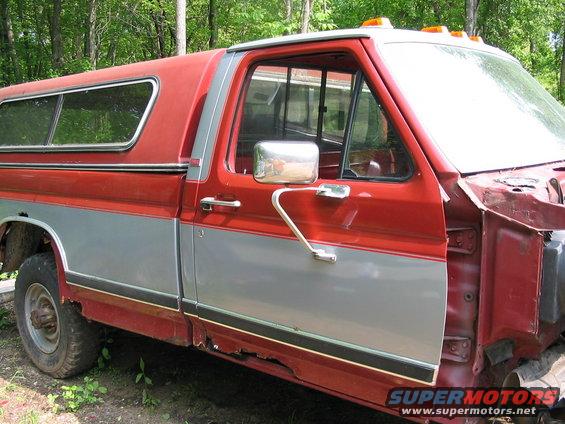 Red and silver pickup truck with a camper shell, showing significant rust on the lower body panels and missing the front fender