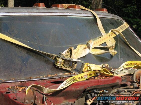 old truck hood with yellow ratchet straps holding it down, some debris on the hood