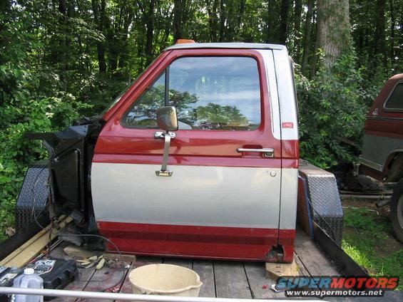 Red and silver Ford F-Series truck cab on a trailer, showing rust damage on the lower door panel