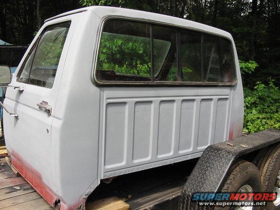 Side view of a gray pickup truck cab, primer showing on lower body, on a trailer