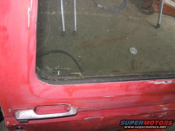 Red truck door with chrome handle and a dirty window. Scratches and rust are visible on the lower body panel