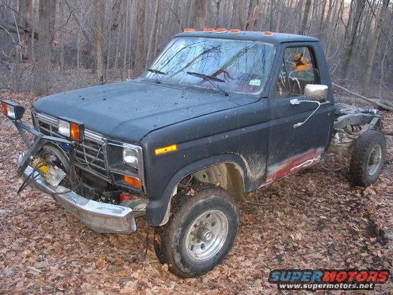 Ford F-Series truck with plow mount, missing rear end, parked in woods