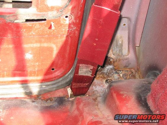 Interior view of a red vehicle's door frame with a red seatbelt and visible rust