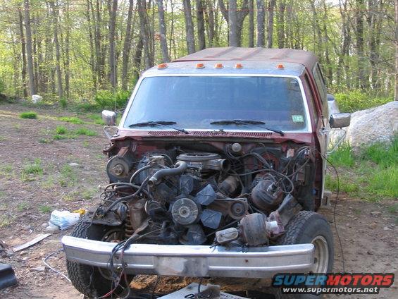 Ford truck missing its engine, parked outside with trees in the background