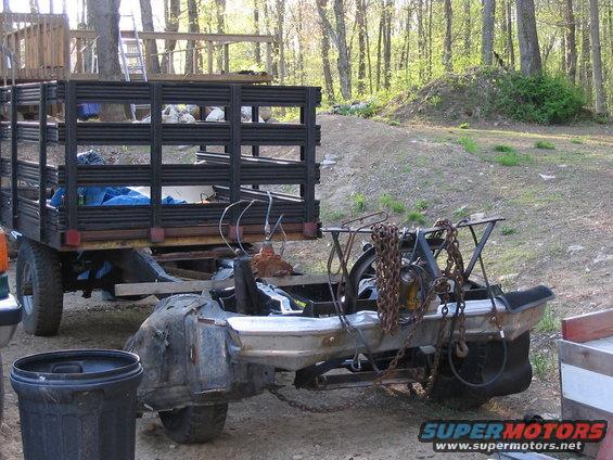 Trailer with black metal racks and a disassembled truck chassis with chains, outdoors