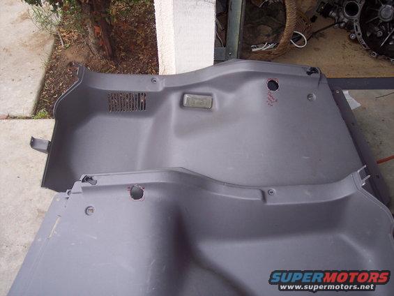 Two gray plastic interior trim panels, possibly from a car's trunk or cargo area, are laid out on a surface