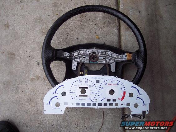 Steering wheel and instrument cluster removed from a vehicle. Gauges show MPH and RPM