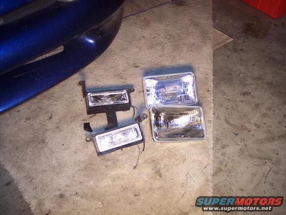 Four headlights on a concrete floor next to a blue car bumper