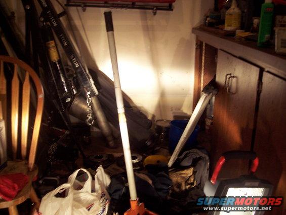 Garage scene with engine hoist, wooden chair, cabinets, and various tools and parts scattered around