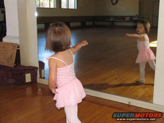 Young child in pink tutu and tights reaches towards a mirror in a dance studio