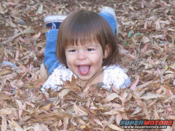 Child lying in autumn leaves, sticking tongue out