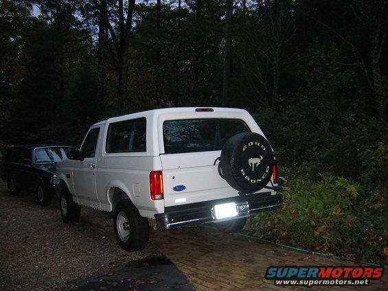 1995 Ford Bronco XL parked next to a dark SUV, spare tire mounted on rear door