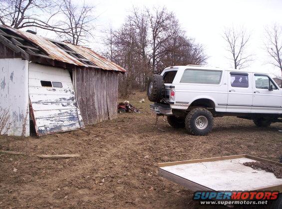 white extended cab pickup truck with spare tire on back parked next to a dilapidated shed