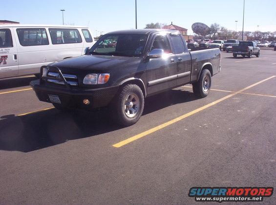 Black Toyota Tundra pickup truck, front 3/4 view, parked in a lot with a white van to the left