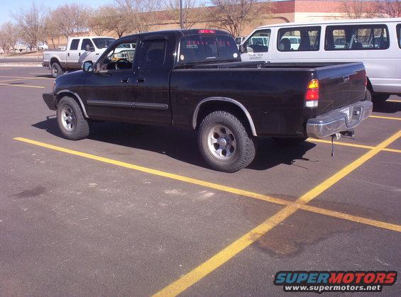 Black pickup truck parked in a lot. Another truck and a van are visible