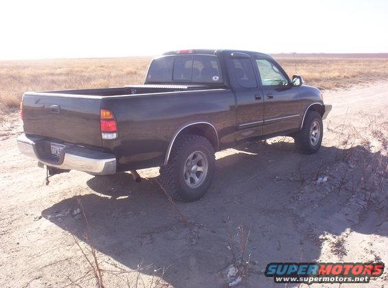 Dark green 2003 Toyota Tundra pickup truck, rear 3/4 view, parked on a dirt road with dry grass