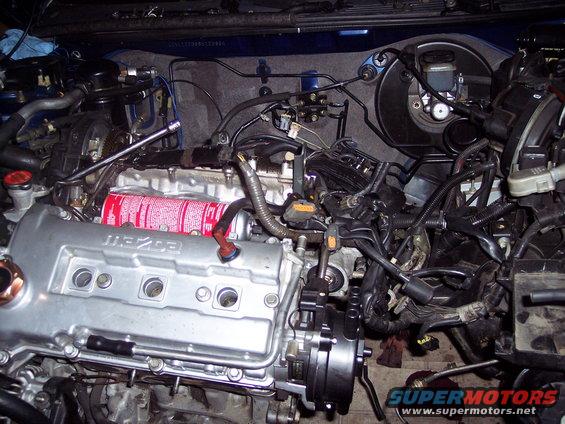 Engine bay with a silver Mazda engine cover, brake fluid reservoir, and various hoses and wires