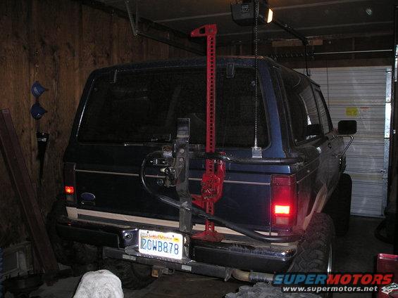 1986 Ford Bronco II parked in a garage with a Hi-Lift jack mounted on the rear spare tire carrier