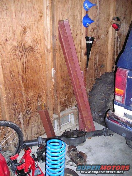 Rear of a blue vehicle, large tire, axle, and blue coil spring in a garage