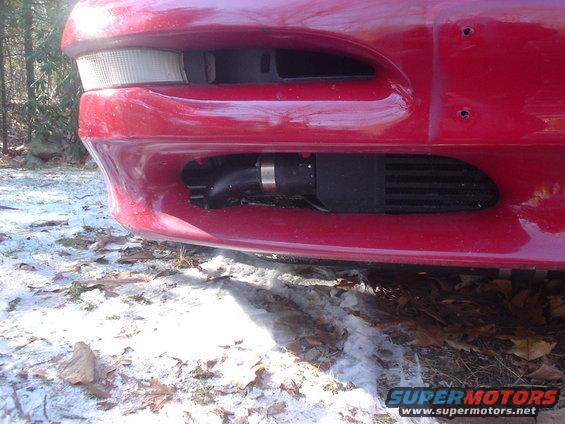 Red car front bumper with visible intercooler and piping. Snow and fallen leaves on the ground